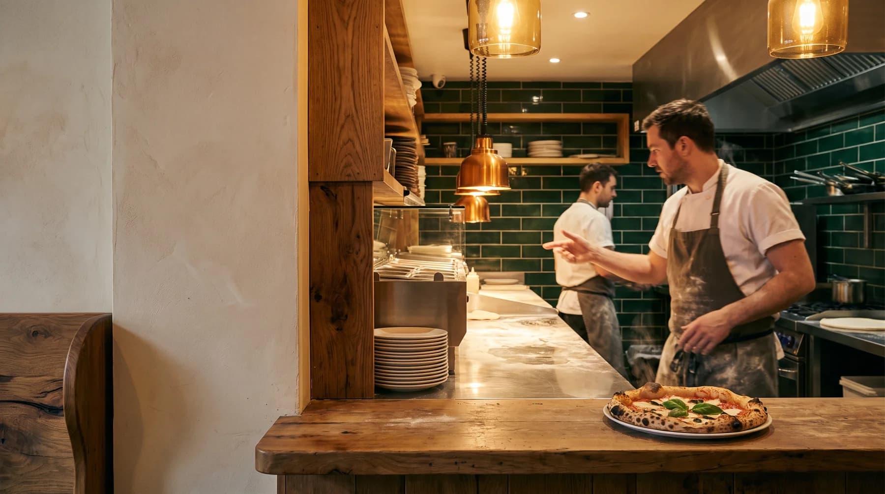 A cook tending the restaurant pass, with a freshly made pizza ready for service